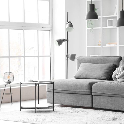Interior of light living room with cozy grey sofa and coffee table near big window Interior of light living room with cozy grey sofa and coffee table near big window